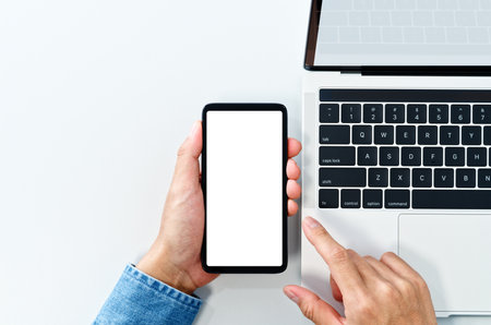 Using smart phone from above. White blank screen. Laptop on white background.