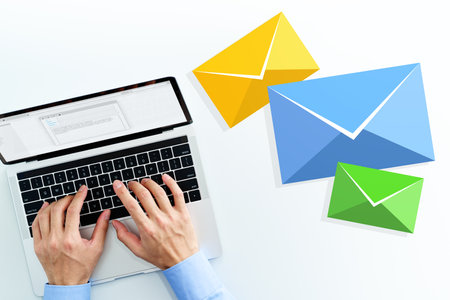 Business man writing email on white table. Top view of using laptop. Three email icons.の写真素材