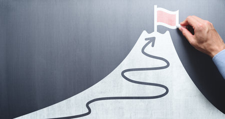 Business goal and success concept. Businessman drawing flag and mountain on chalkboard.の写真素材