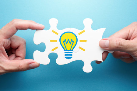 Inspiration and solution. Two hands connecting jigsaw puzzle pieces. Illustration of light bulb.の写真素材