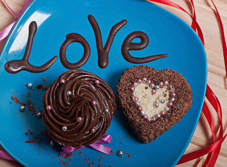 Chocolate cupcakes with chocolate cream and cupcake in the shape of heart, decorated with ribbon, on a wooden background. Valentine's Day.の写真素材