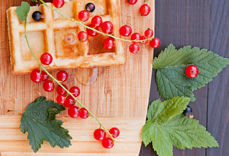 Belgian waffles decorated with red currants on a wooden background, natural product, food - dessert, pastry with fruit.の写真素材