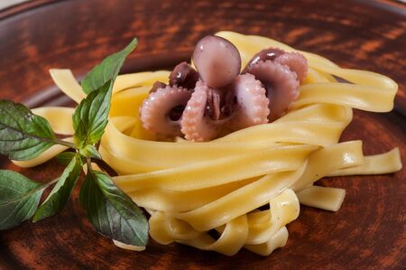 Seafood Fettuccine pasta with octopus, garnished with basil on a clay plate and fabric background.の写真素材