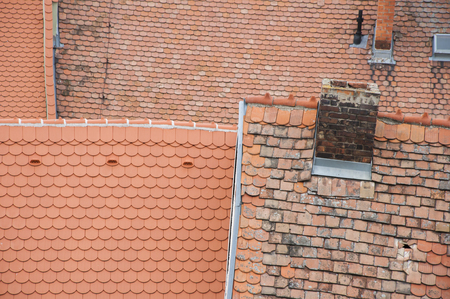 Closeup of roof orange shingles with chimney on top of roof.