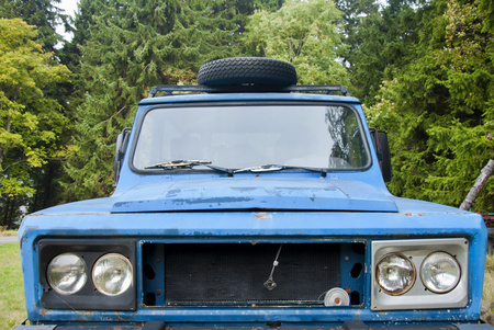 Blue old rusty SUV car parking on the meadow. Close up of blue offroad.