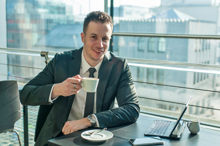 Young businessman in suit working in office. Cup of coffee, smartphone and laptop is on black table.の写真素材