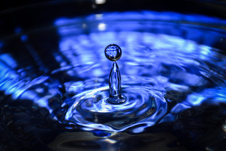 Falling water drop into water making crown. Close up of a blue water drop, macro photography.の写真素材
