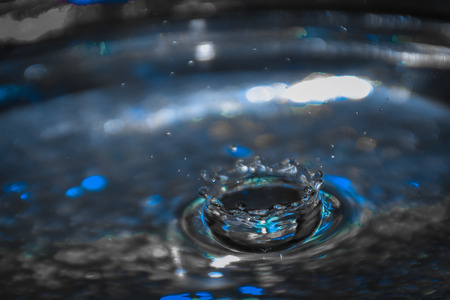Falling water drop into water making crown. Close up of a blue water drop, macro photography.