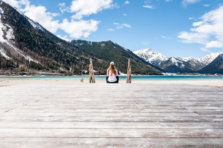 Young woman sitting on jetty. Pretty lady sitting on pier by the lake in the Alps mountains.の写真素材