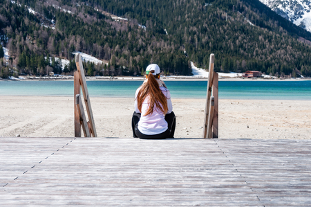 Young woman sitting on jetty. Pretty lady sitting on pier by the lake in the Alps mountains.の写真素材