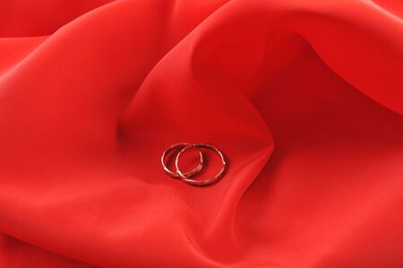 red graceful fabric and  gold wedding rings close upの写真素材