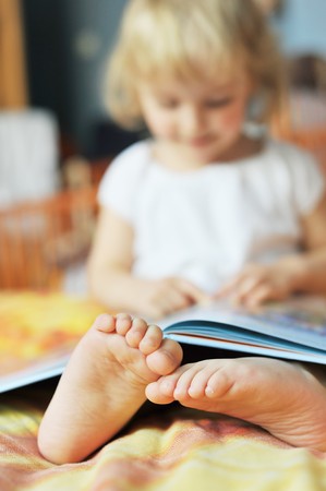 cheerful little girl with book sits on bed of parentsの写真素材