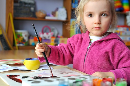 Beautiful little girl is drawing with gouaches on paperの写真素材