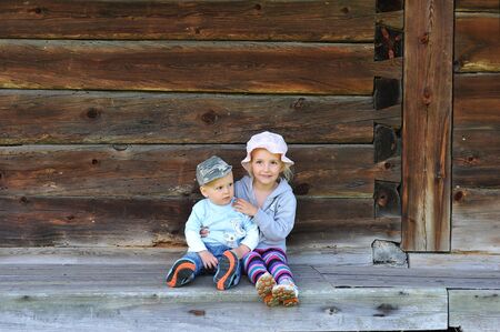 Brother and sister sitting near wooden wall of houseの写真素材