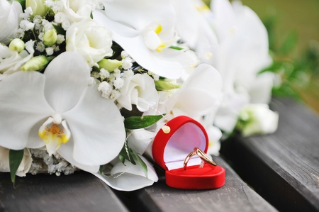 bouquet of white orchids and wedding gold rings on wooden bench 