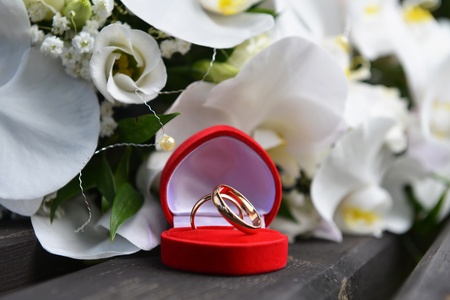 bouquet of white orchids and wedding gold rings on wooden bench 