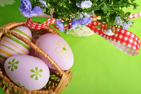wicker basket of easter eggs with blue campanula flowers  on green background