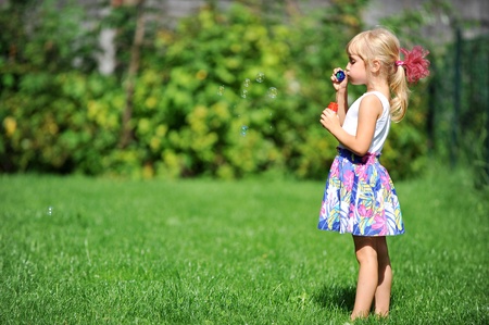 little girl play with bubble blower on green lawnの写真素材