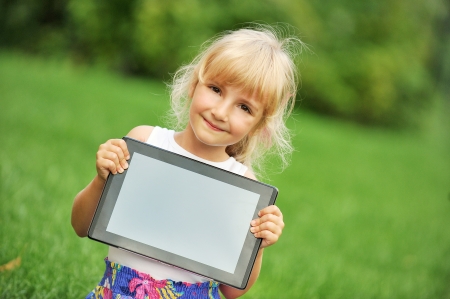 beautiful and happy little girl sitting on grass with laptop computerのeditorial素材