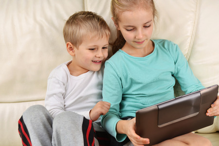 girl with brother using  tablet sits on sofaの写真素材