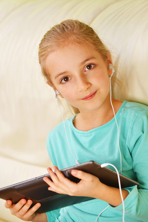 girl using a tablet with headphones sits on couchの写真素材