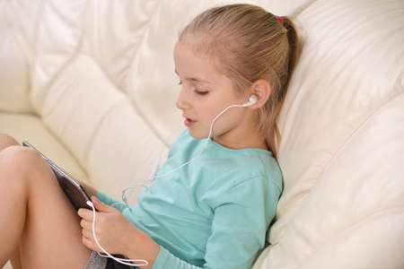 girl using a tablet with headphones sits on couchの写真素材