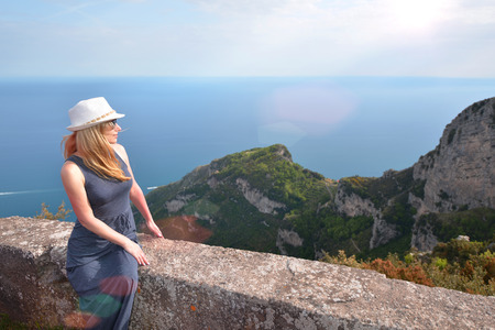 Woman in hat sits on stone fence of mountain roadの写真素材