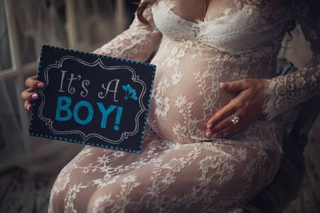 The future mother poses with her belly and the sign she writes on  its a boy