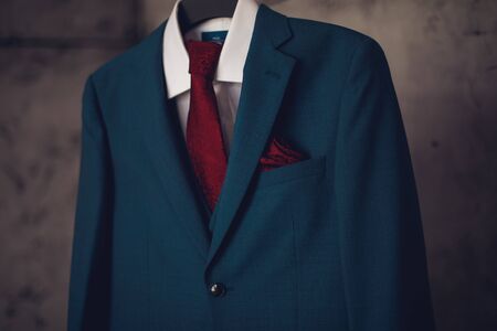 A blue suit with a red tie on a hanging hanger is waiting to be wornの写真素材