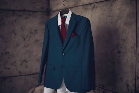 A blue suit with a red tie on a hanging hanger is waiting to be wornの写真素材
