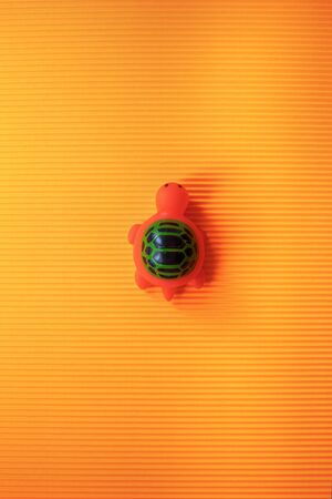 Orange toy turtle with green shell on textured orange background. High quality photoの写真素材