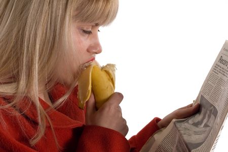 Young blondie girl reading newspapers and eating bananaの写真素材