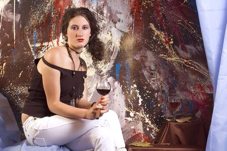 Young brunette sitting in art studio with glass of red wine and cigarの写真素材