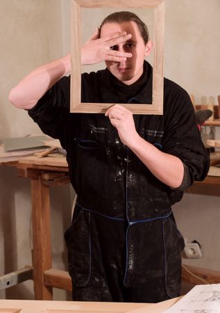 Young carpenter gesturing with hands and holding frame in his workshopの写真素材