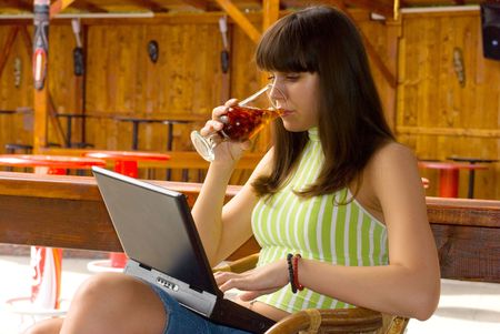 Young woman sitting in restaurant, drink a juice and ding chat with laptopの写真素材