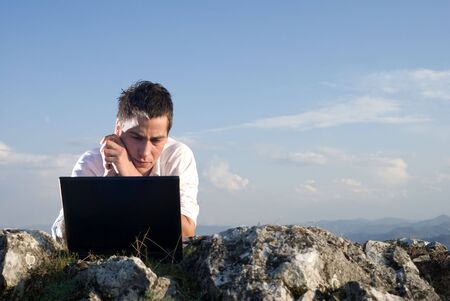 Young man using his laptop, sitting on the  rocky    の写真素材