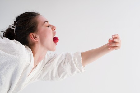 Woman holding a strawberry in mouth with bioenergy with her handsの写真素材