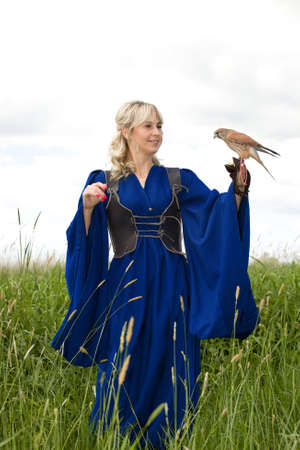 beautiful girl in a long blue medieval dress with a hunting Falcon on her gloveの写真素材