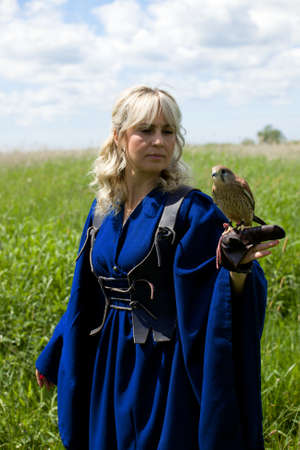 beautiful girl in a long blue medieval dress with a hunting Falcon on her gloveの写真素材
