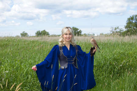 beautiful girl in a long blue medieval dress with a hunting Falcon on her gloveの写真素材