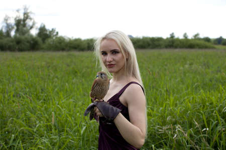 a girl with blonde hair in a dress holds a Kestrel on her armの写真素材
