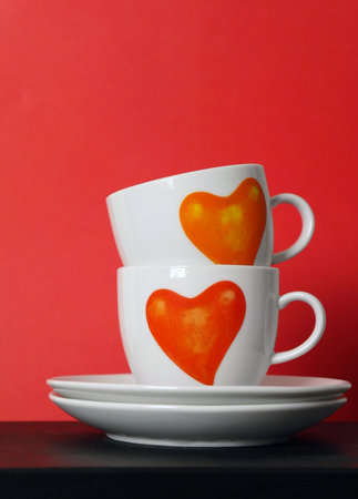 Two white tea cups with painted red hearts on red background, selective focus,copy spaceの写真素材