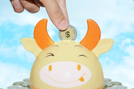Saving  Money concept,  Woman hand putting coin into cute baffalo bank on blue skyの写真素材