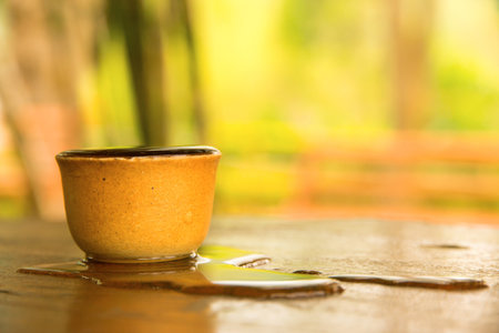 clay cup full with water overflow on tableの写真素材