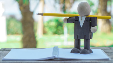wooden doll of businessman thinking an idea with his pencil and notebook paper, business concept