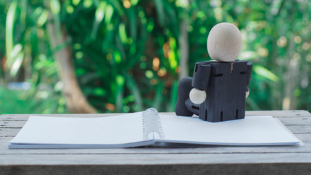 wooden doll of businessman sitting and thinking with notebook on nature background , business conceptの写真素材