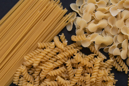 Italian pasta on black background. Farfalle, fusilli and spaghetti.
