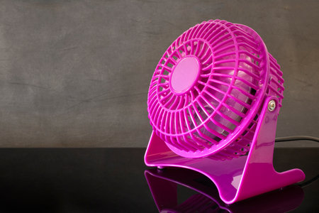 Pink mini fan working on black table.の写真素材