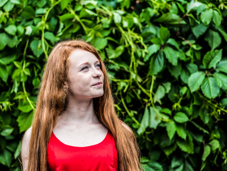 Beautiful red-haired girl with freckles on the green backgroundの写真素材
