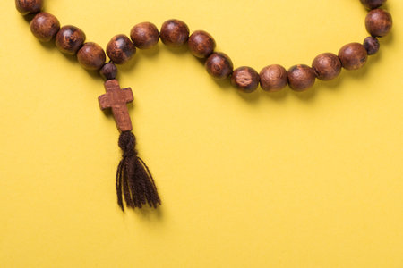 Wooden rosary and cross on yellow background.の写真素材